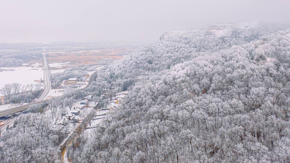 Aerial panorama of a snowy, foggy morning over bluffs and backwaters of the Mississippi River at La Crosse, Wisconsin at the intersection of a busy highway, railroad tracks, Myrick Marsh Hixon Forest.