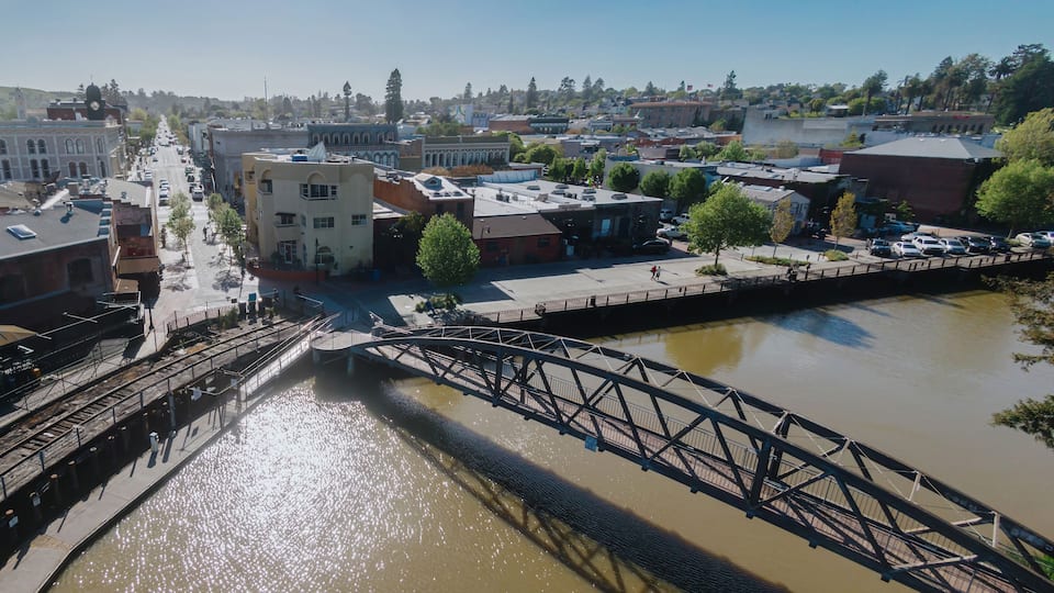 A river with a bridge, buildings, and a train track.