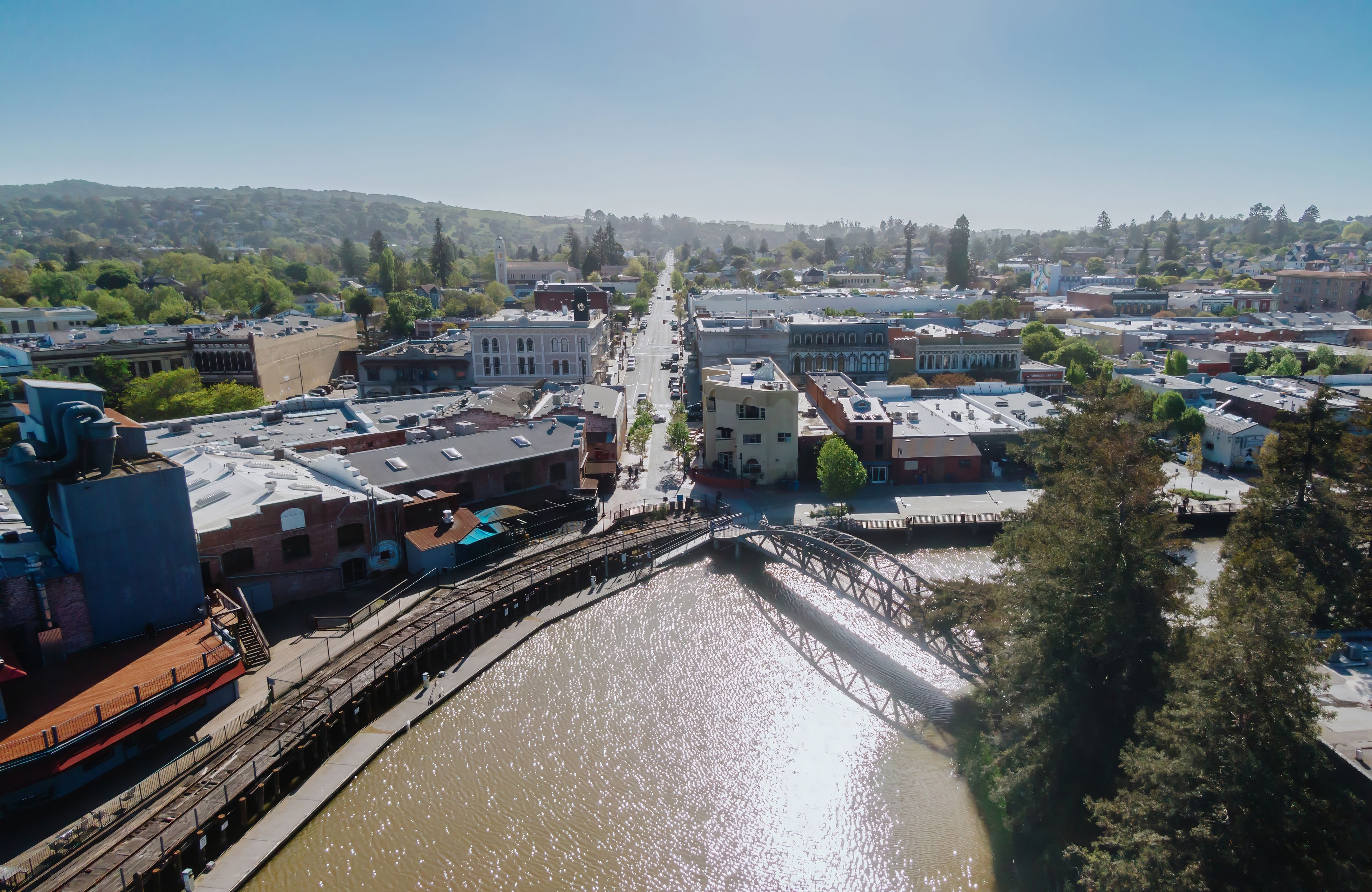 A river with a bridge, buildings, and a hilly landscape in the background.
