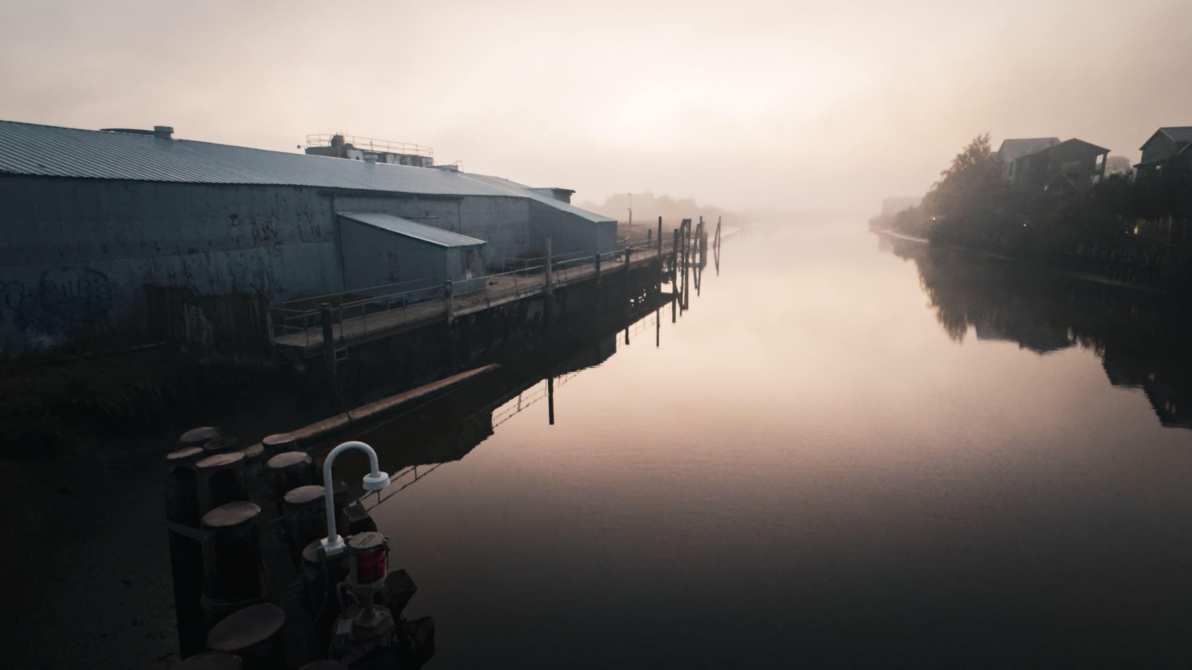 A foggy waterfront with industrial buildings and a calm river.