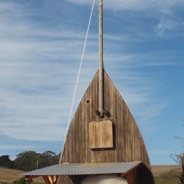 A wooden barn with a pointed roof and a metal pole.