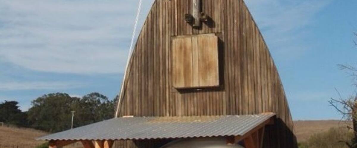 A wooden barn with a pointed roof and a metal pole.