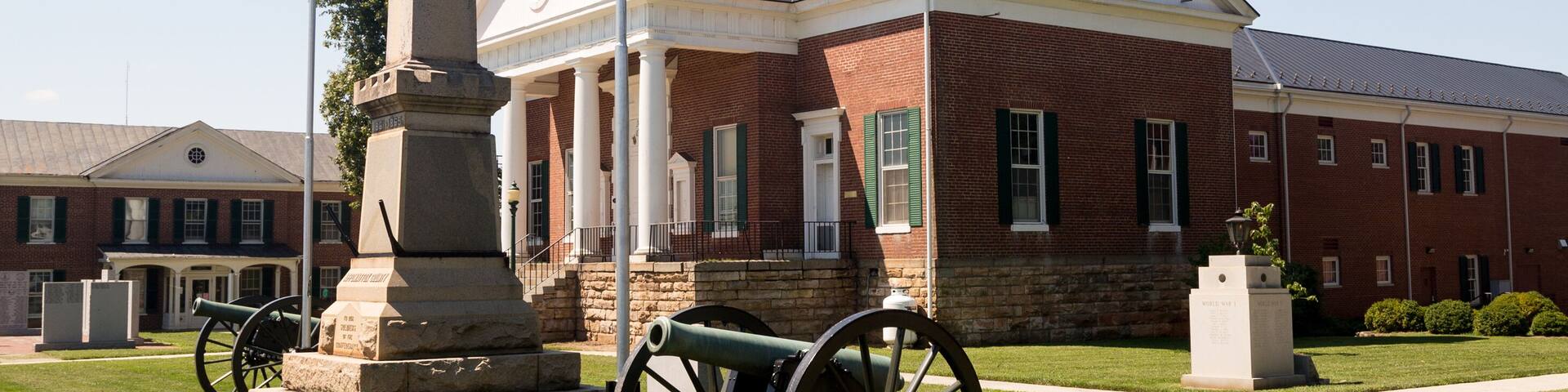 A historic building with a clock tower, a statue, and a cannon.