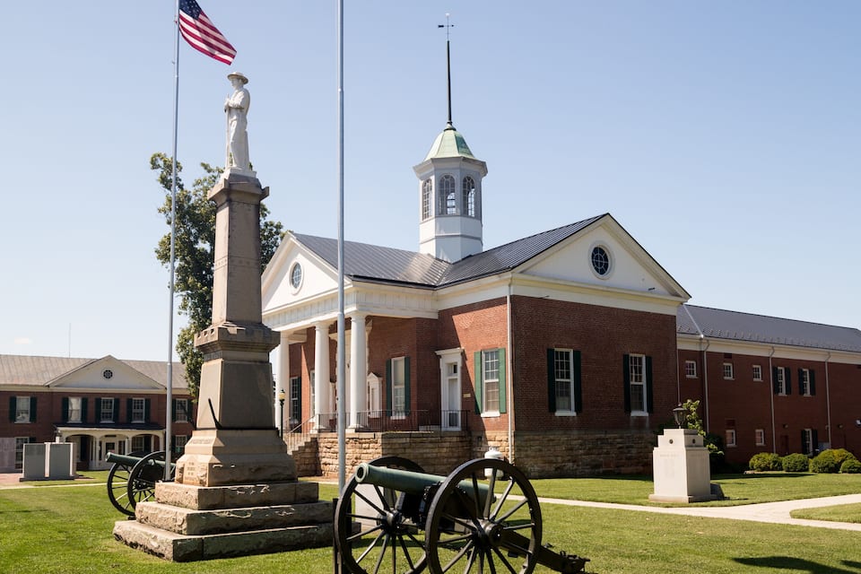 A historic building with a clock tower, a statue, and a cannon.