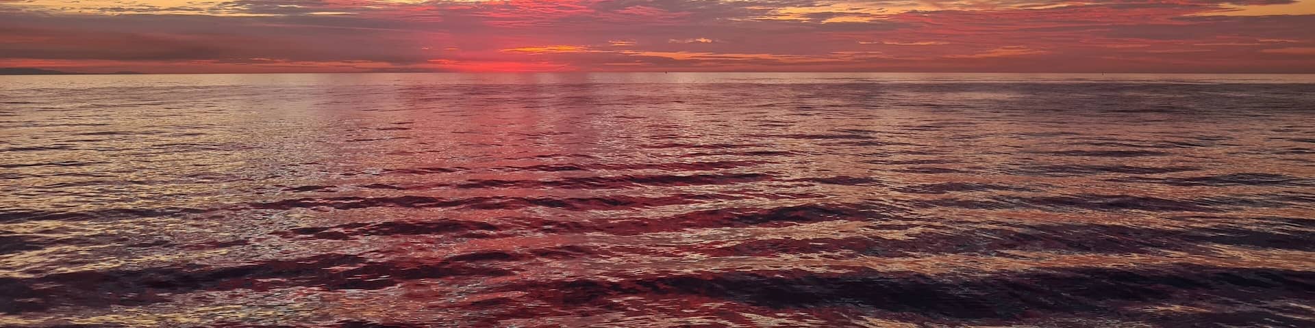 The first signs of sunrise against the background colored clouds and calm surface of the sea
