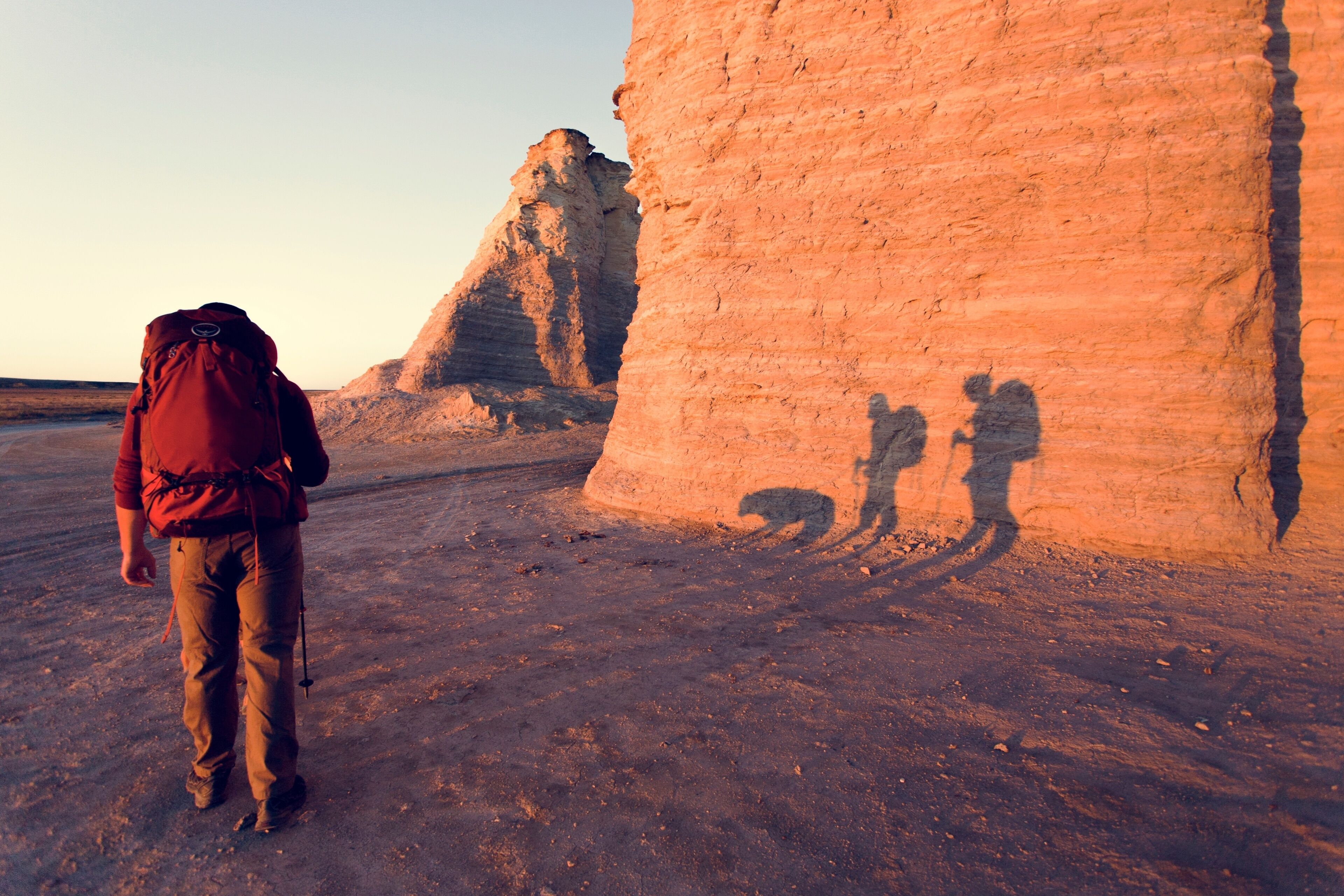 A person walking towards a large rock formation with a backpack.