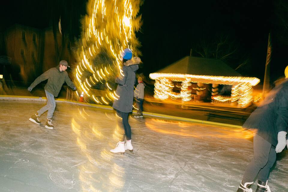 People ice skating on a rink with illuminated structures in the background.