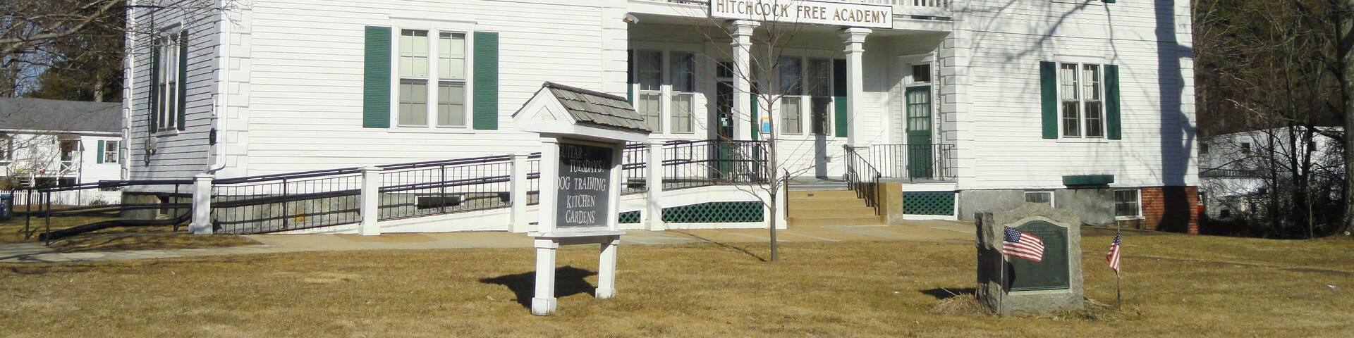 A white building with green shutters, a porch, and a sign reading "Hitchcock Free Academy".