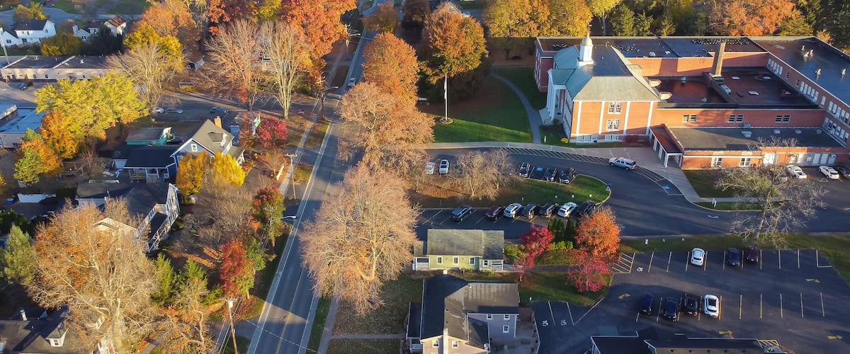An aerial view of a residential area with autumn-colored trees, a main road, and a large building with a pointed roof.