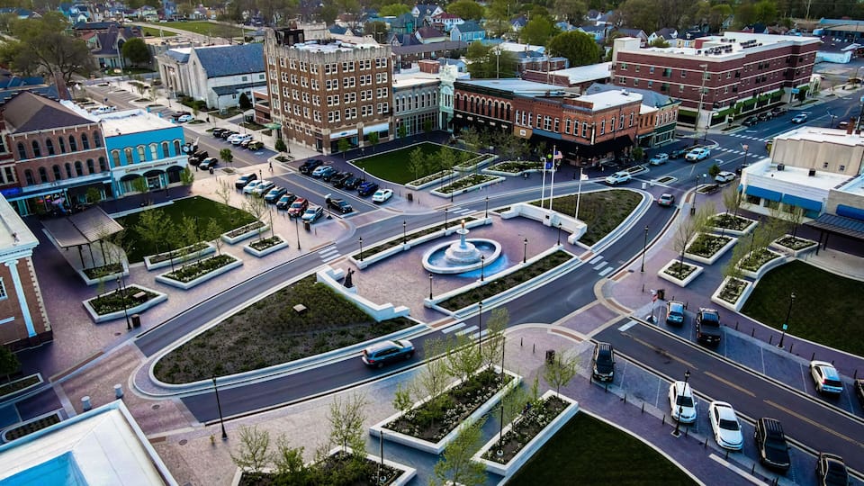 A city intersection with a roundabout, surrounding buildings, and a central landscaped area.