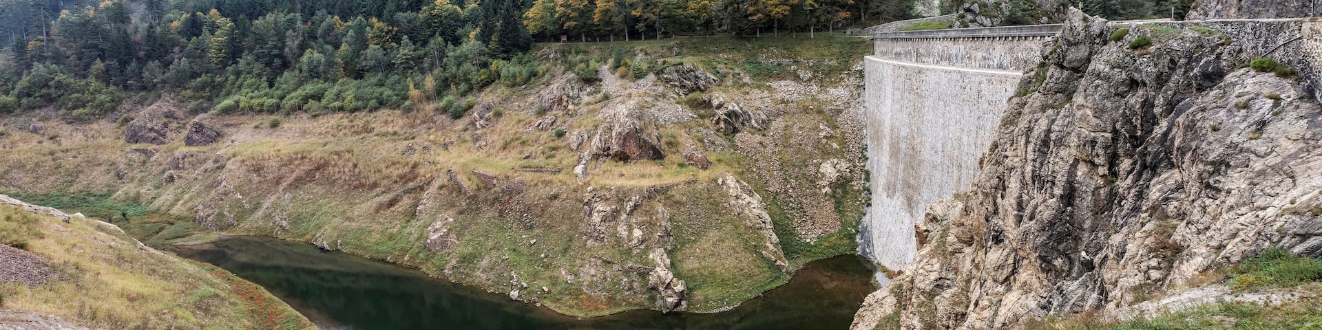 A dam with a river flowing through a valley, surrounded by forested hills.