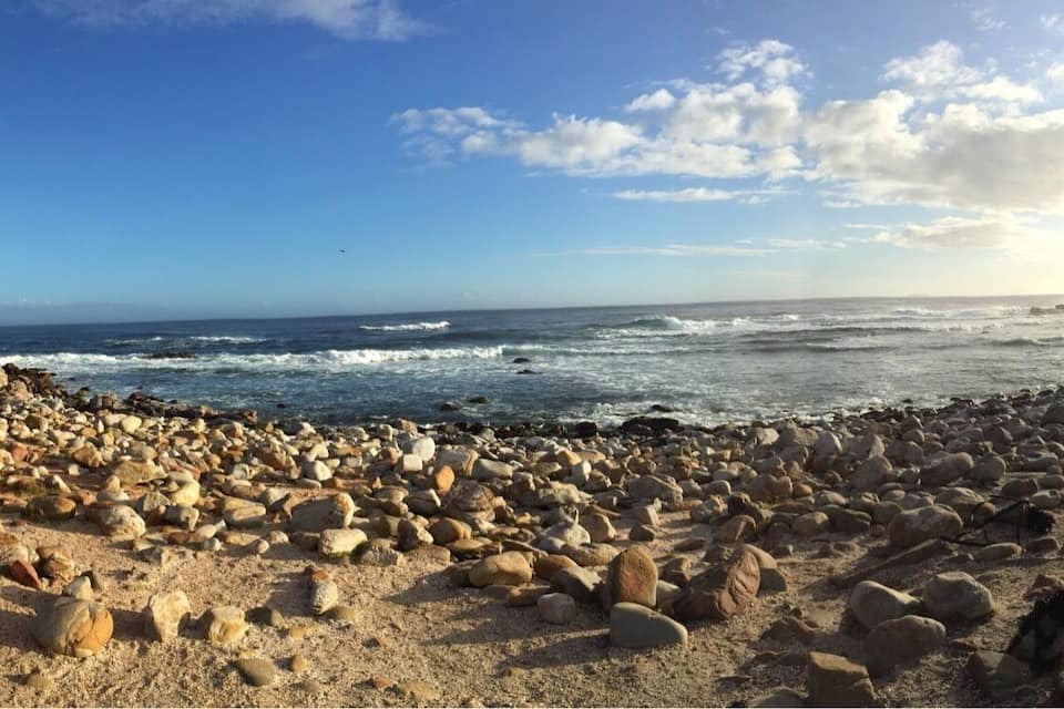 Litoral rochoso com uma grande formação rochosa à esquerda e o oceano ao fundo.