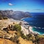 A coastal landscape with a rocky cliff, a beach, and a town by the sea.