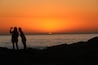 Twee silhouetten van mensen voor een ondergaande zon boven de oceaan.