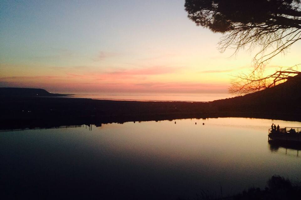 Um pôr do sol sobre um lago calmo, com silhuetas de árvores e um barco.