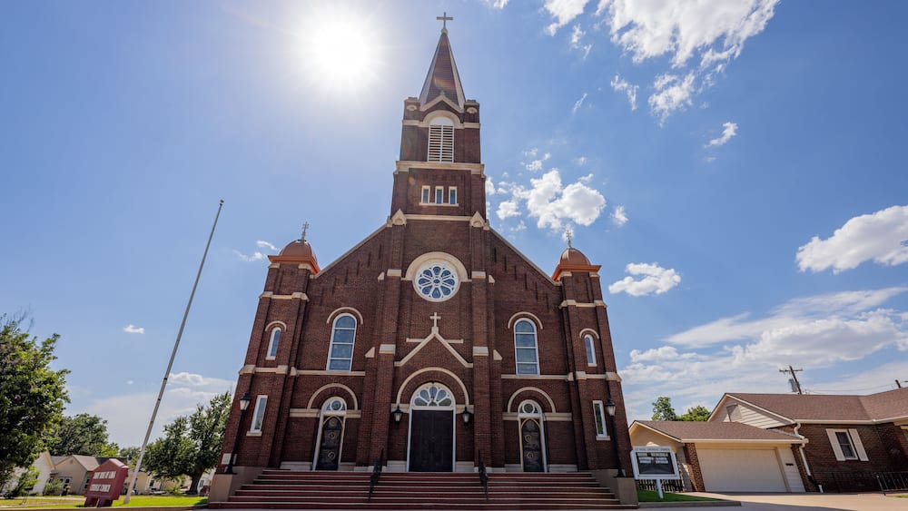 A large brick church with a tall steeple and a cross on top, under a clear blue sky.
