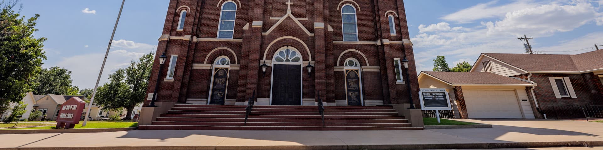 A large brick church with a tall steeple and a cross on top, under a clear blue sky.