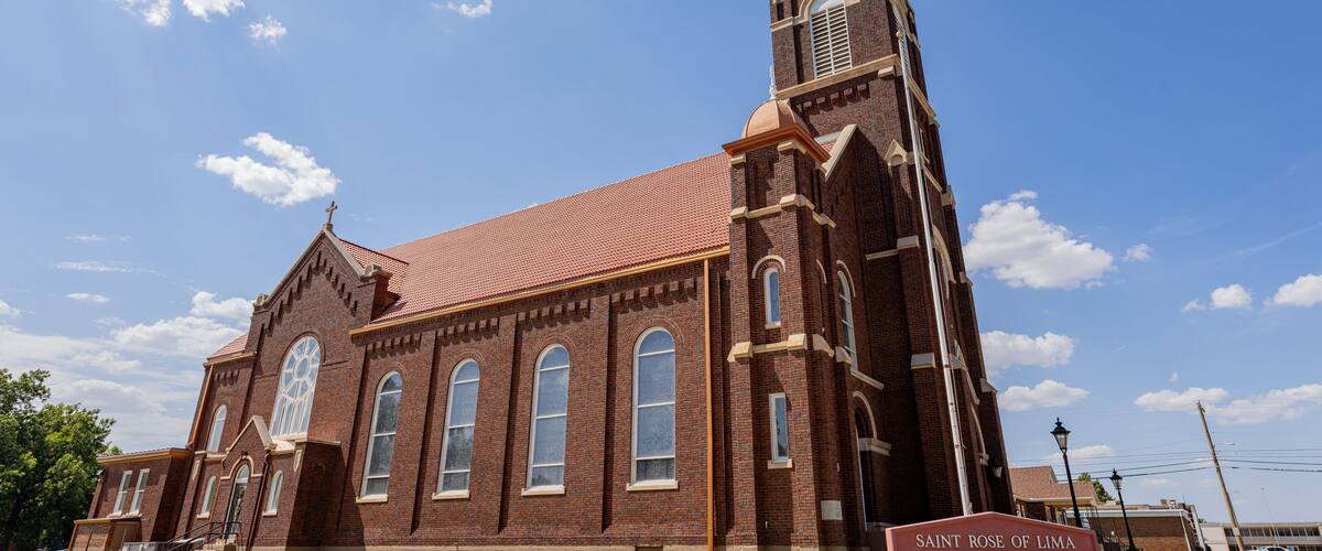 A brick church with a tall steeple and a sign reading "Saint Rose of Lima Catholic Church".