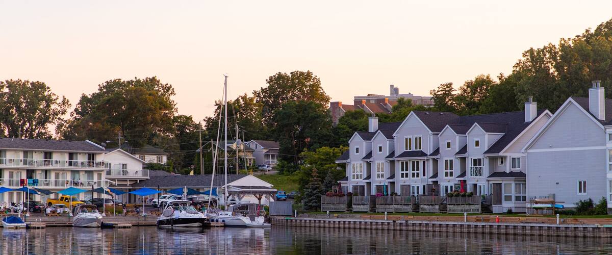 A marina with boats docked, waterfront houses, and a sunset sky.