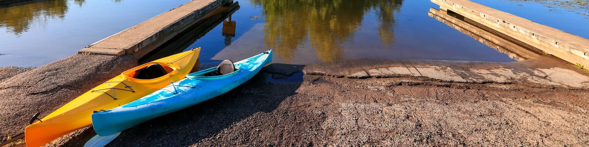 A calm lake with a dock, two kayaks, and a small island with trees.