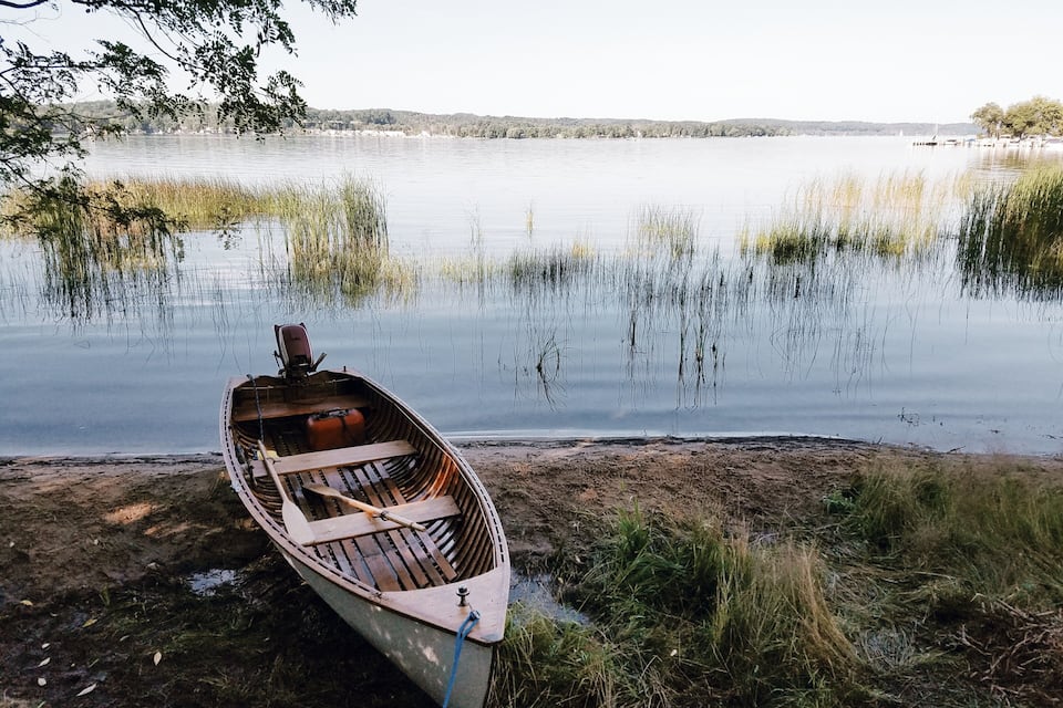 A wooden boat on a calm lake with reeds and trees in the background.