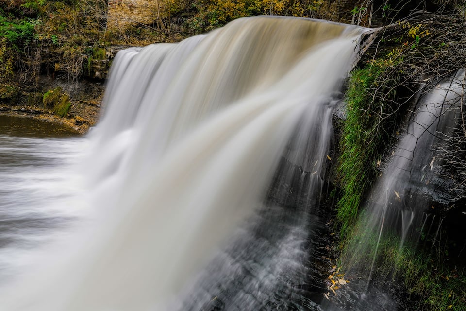 A waterfall cascading over a rocky cliff surrounded by greenery.