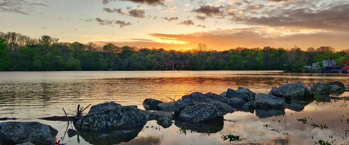 Aerial view of lake surrounded by growing lush green trees in Griggs reservoir park during sunset