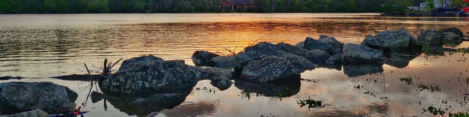 Aerial view of lake surrounded by growing lush green trees in Griggs reservoir park during sunset