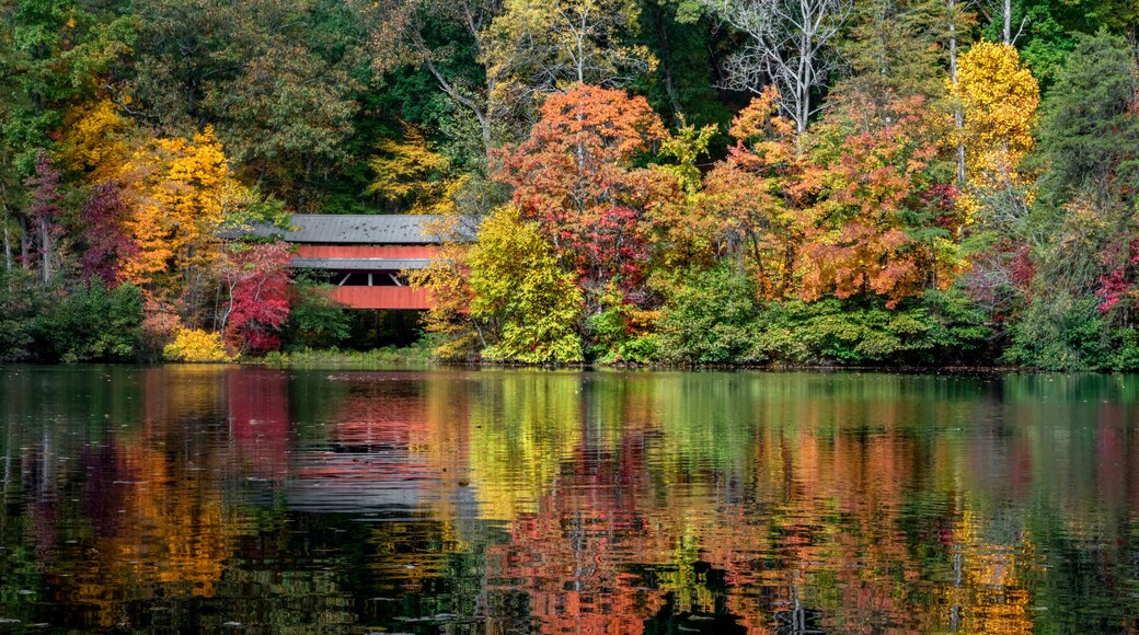 With a beautiful reflection on Lake Loretta in Alley Park, Lancaster, Ohio, the red George Hutchins Covered Bridge, surrounded by colorful autumn leaves, was constructed in 1865 at another location.