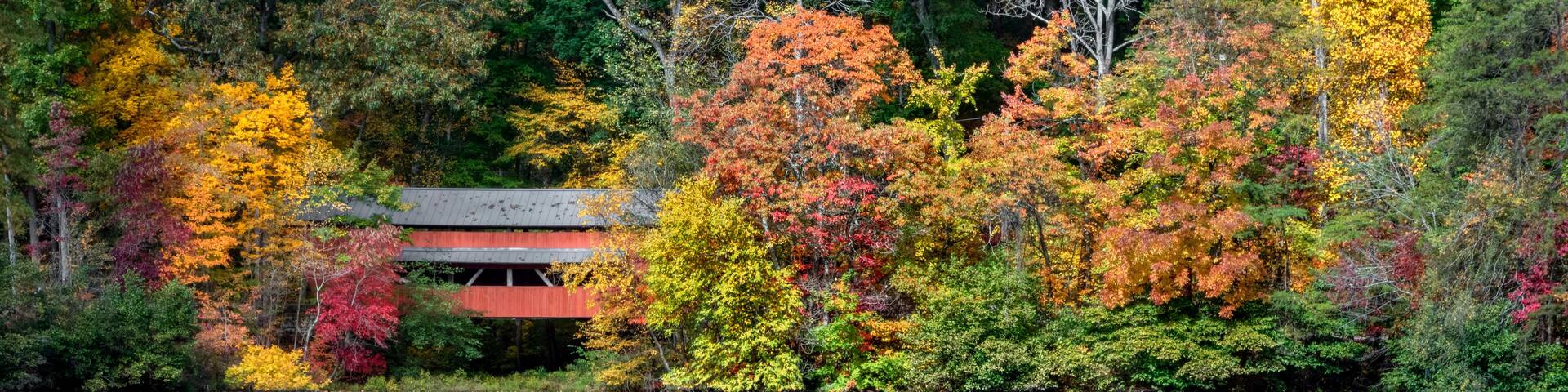 With a beautiful reflection on Lake Loretta in Alley Park, Lancaster, Ohio, the red George Hutchins Covered Bridge, surrounded by colorful autumn leaves, was constructed in 1865 at another location.