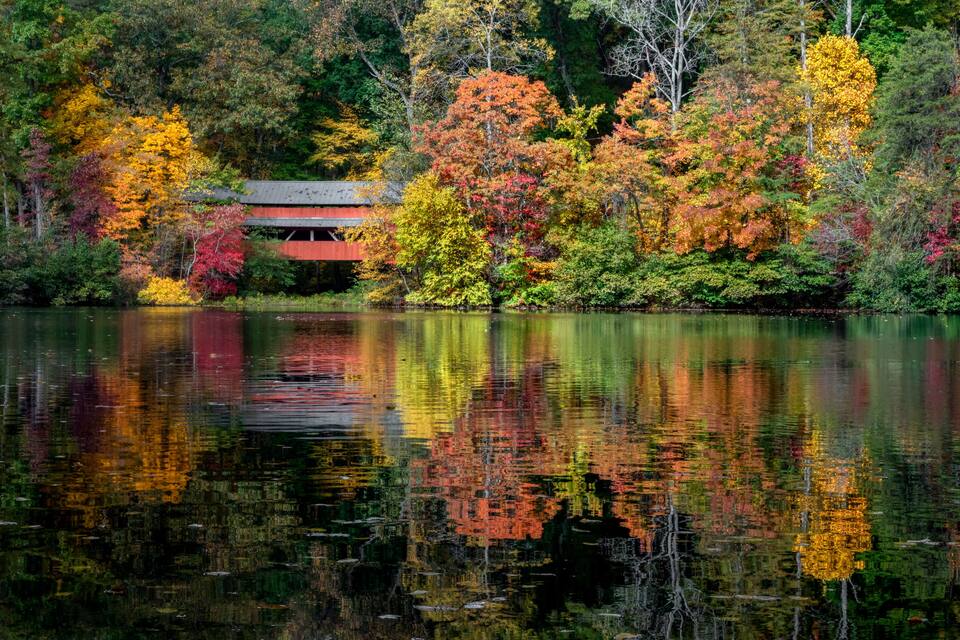 Un lago con follaje otoñal, un edificio de techo rojo y reflejos en el agua.