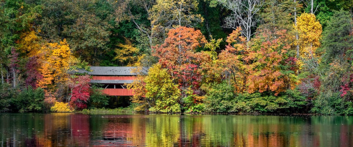 A lake with autumn foliage, a red-roofed building, and reflections on the water.