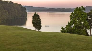 A calm lake with a boat, surrounded by grassy hills and trees.