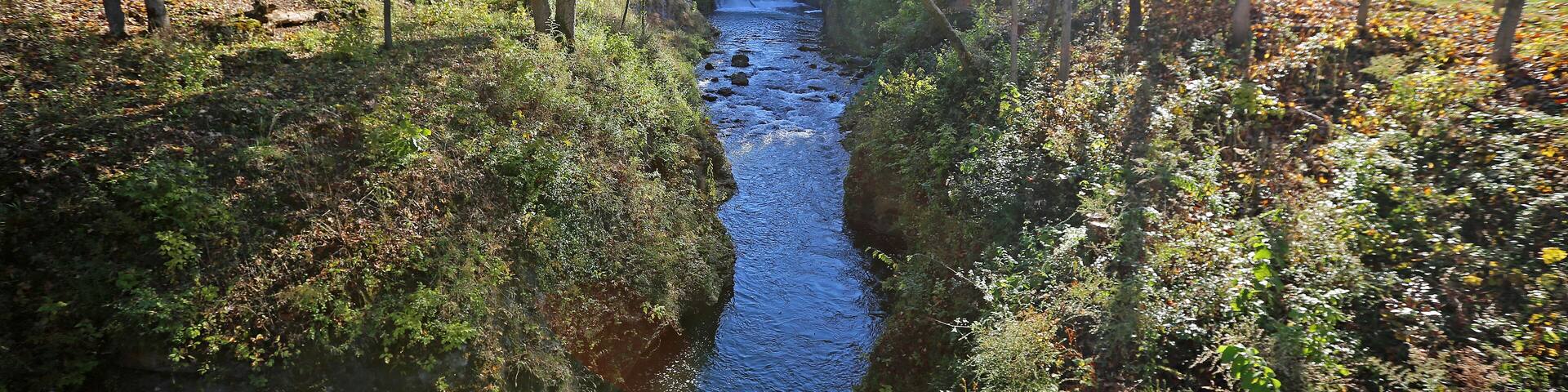 A waterfall in a forested area with a wooden bridge.
