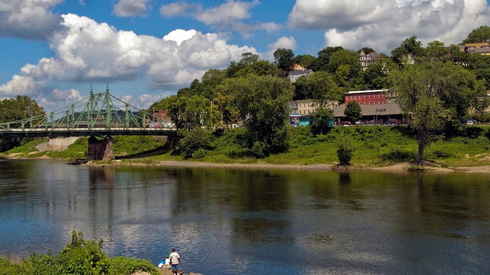 A river with a bridge, green hills, and buildings in the background.