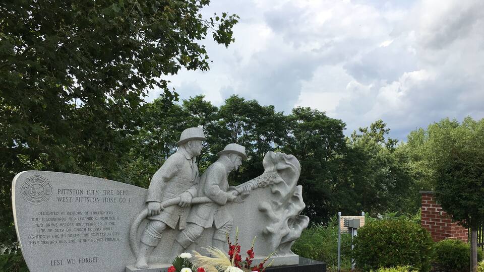 A memorial statue of firefighters with a plaque and flowers.