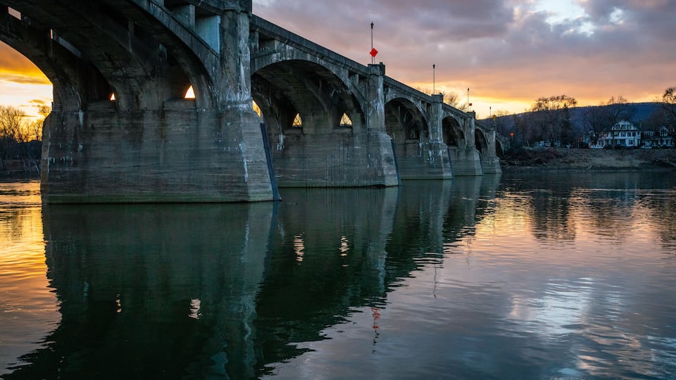 A large stone bridge over a calm river at sunset.