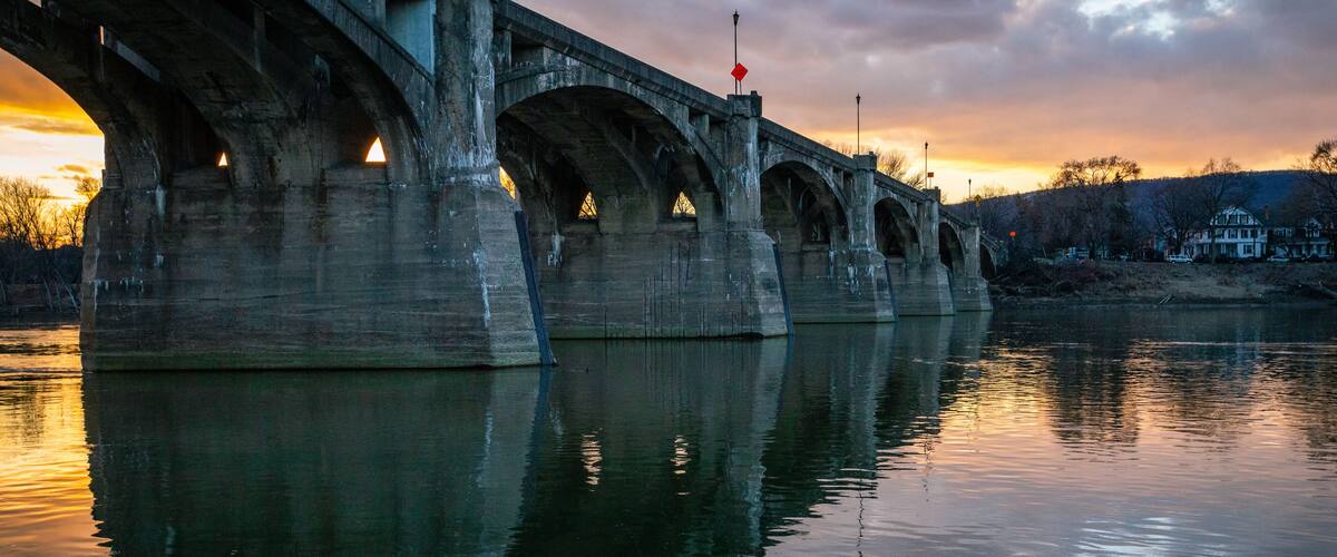 A large stone bridge over a calm river at sunset.