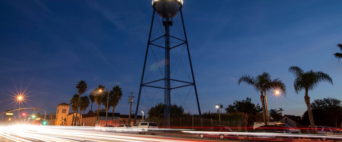 A water tower at dusk with light trails from vehicles on the road.