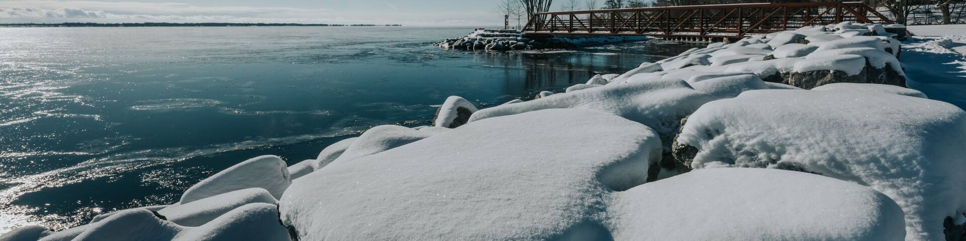 Large snow covered rocks on edge of lake on sunny winter day.