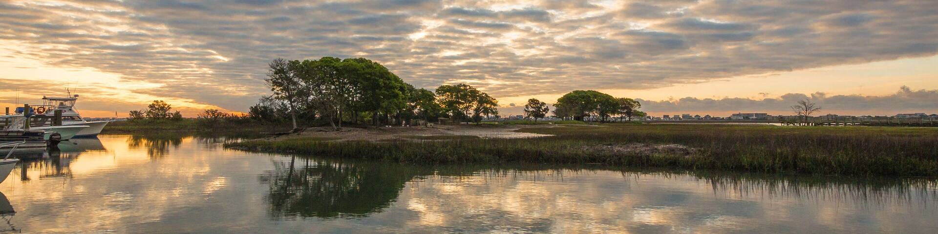 A calm lake with boats, trees, and a sunset sky.