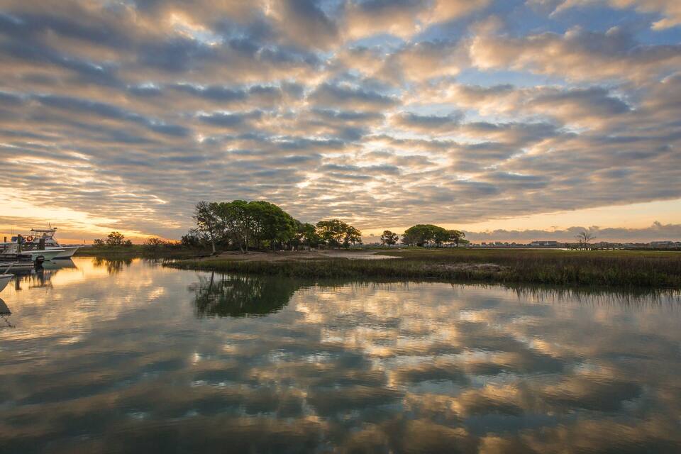 A calm lake with boats, trees, and a sunset sky.