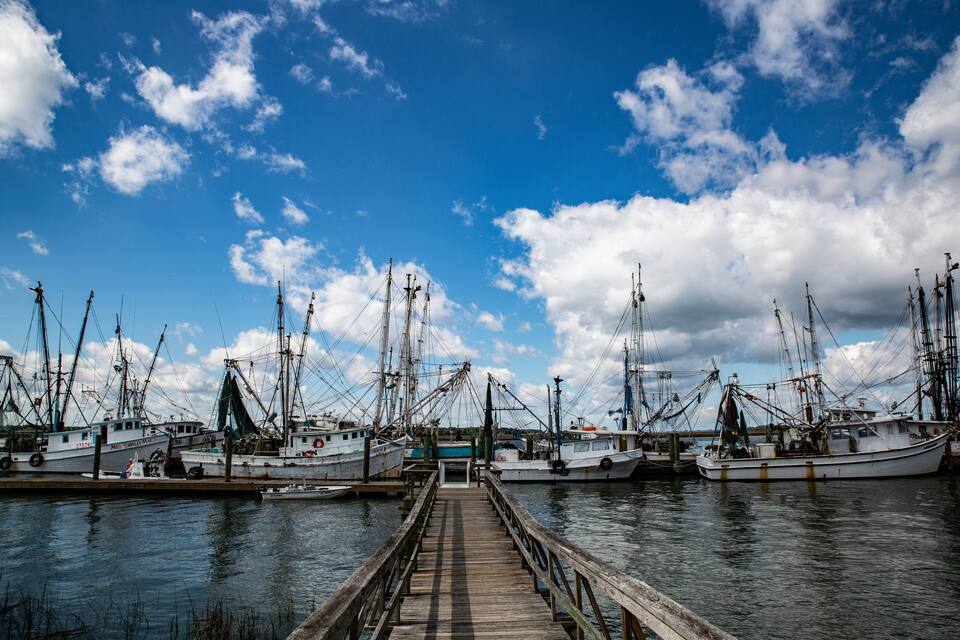 A harbor with several fishing boats docked at wooden piers under a partly cloudy sky.