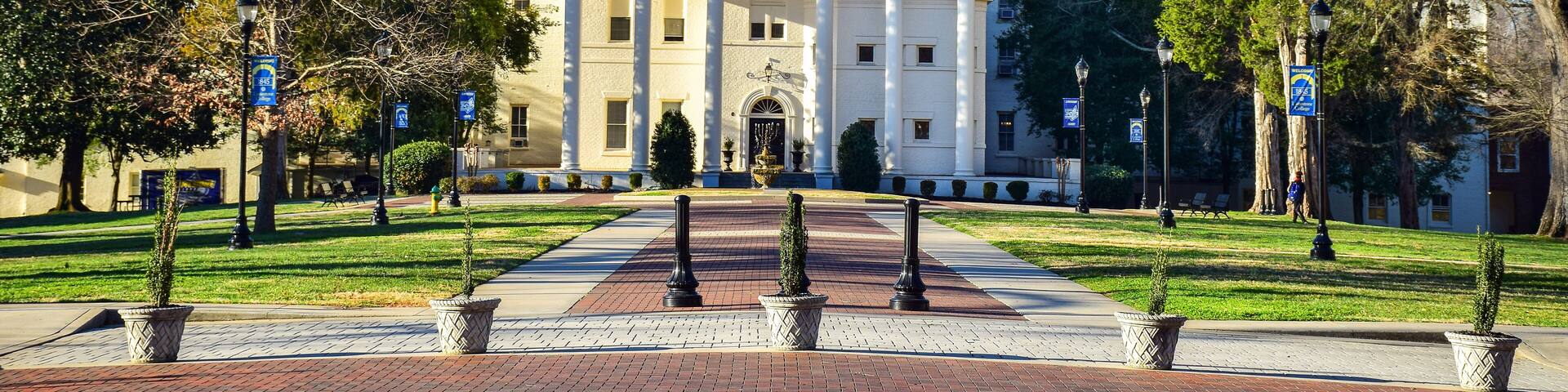 Limestone College's main building with a clock tower, surrounded by trees and a paved walkway.