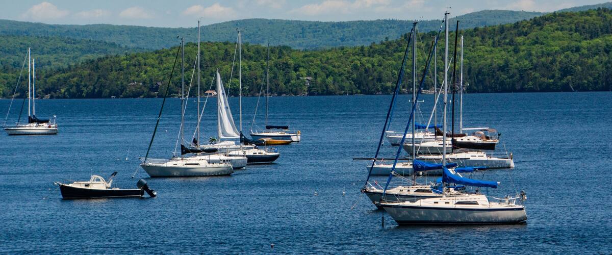 A marina with several sailboats docked in calm waters, surrounded by lush green hills.