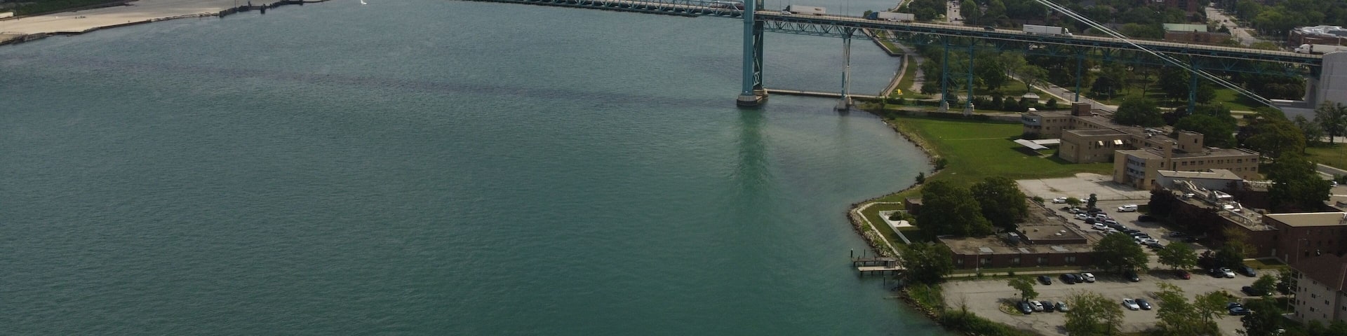 A large suspension bridge spanning a wide river, with a city skyline in the background.