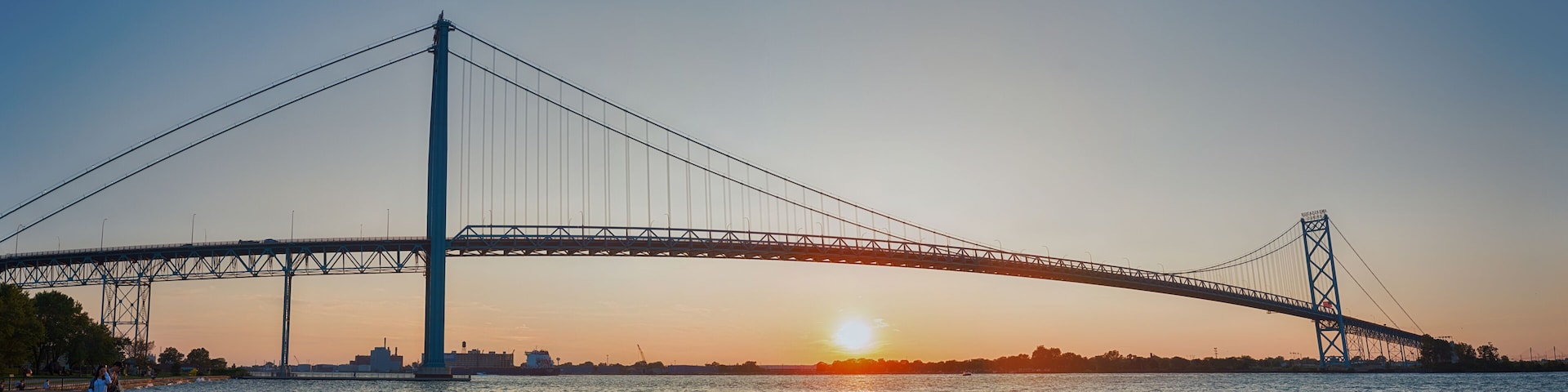 Eine Hängebrücke im Abendlicht, die Sonne geht am Horizont unter.