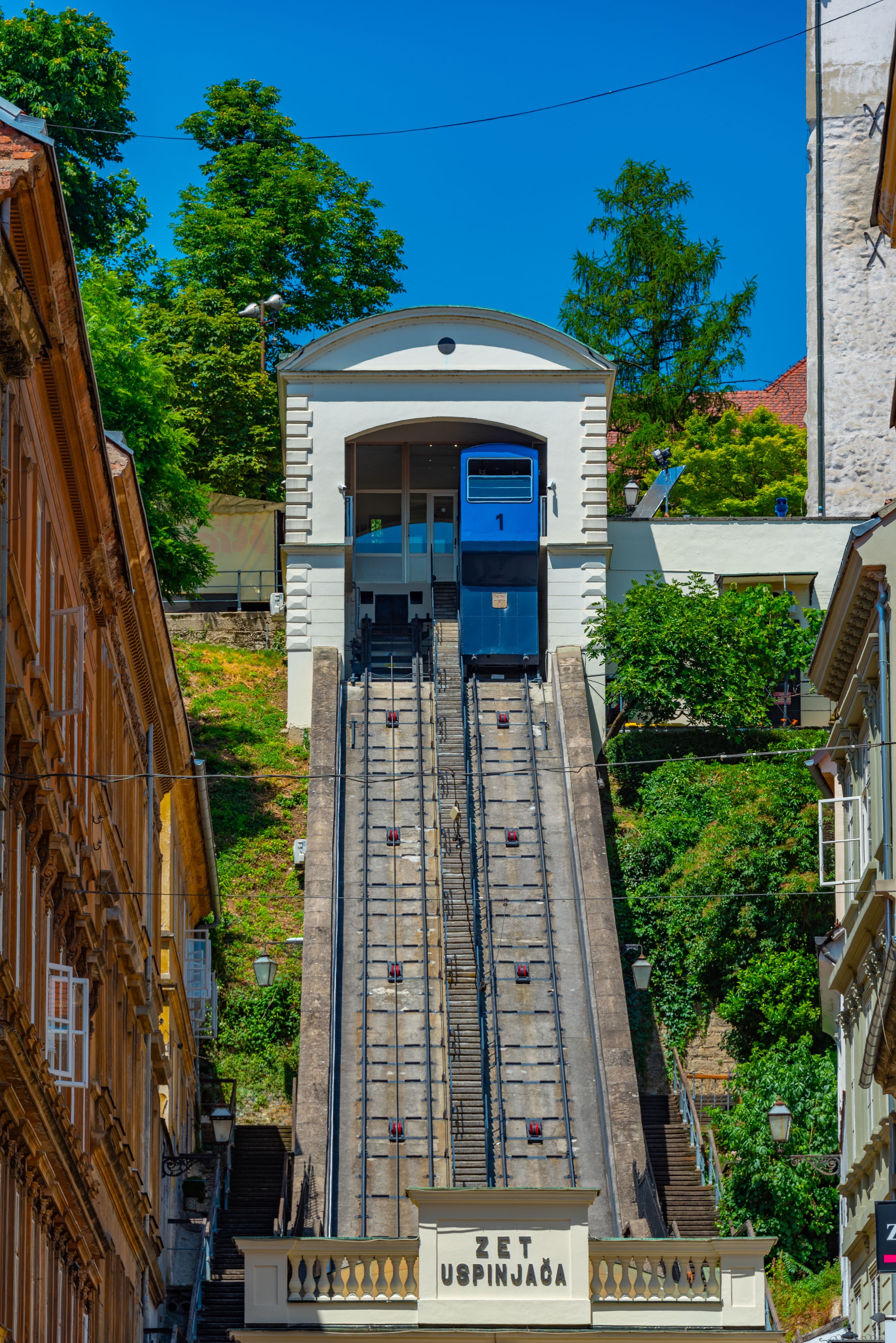 Un tramway gravissant une pente abrupte, entouré d’une végétation luxuriante et d’édifices historiques.