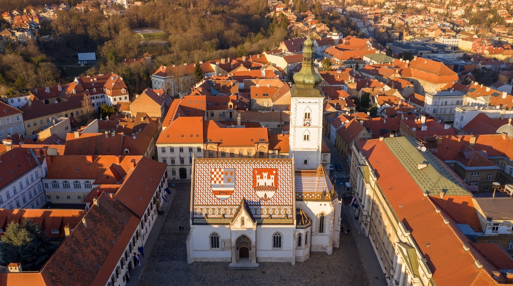 Une ville historique aux bâtiments aux toits rouges, une église imposante dotée d’un clocher et une grande place avec un toit à motifs.