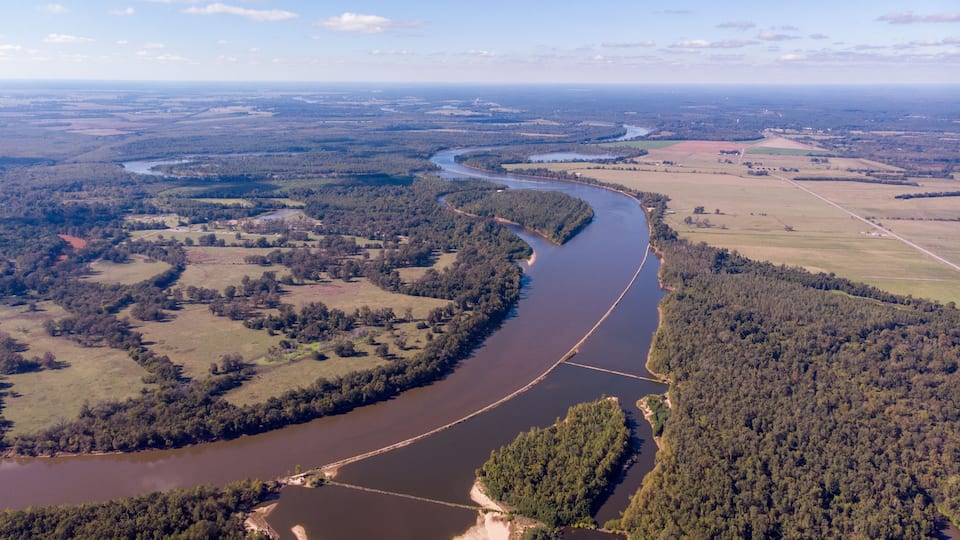 A river winding through a forested landscape with fields and a distant view of the horizon.